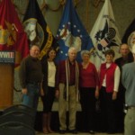This veteran proudly wears his scarf and gets a picture snapped with his family in front of the service flags.