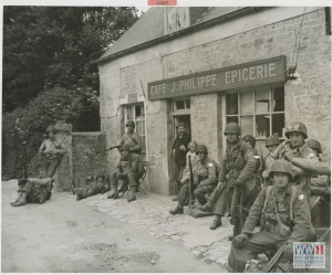 "Exhausted from their rapid advance inland from the Normandy beachhead, U.S. soldiers relax for a few minutes outside of a French cafe." 20 June 1944. U.S. Navy Official photograph, Gift of Charles Ives, from the collection of the National WWII Museum. 2011.102.386