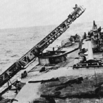 View looking aft showing the damage to the starboard catapult after the first torpedo hit. 
US Navy Official photograph.