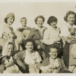 Eight women Red Cross workers; some holding jackets and other parts of uniforms, one holding a small dog or puppy, probably on Tinian in 1945. Gift of David Lawrence, from the collection of the National WWII Museum.