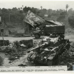 A US truck passes behind a disabled German tank in France about a month after D-Day.