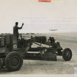 A Seabee working on the runway at Tinian as a B-29 lands.